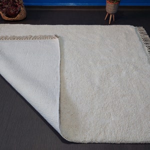 May include: A white, fluffy rug with a fringe border. The rug is folded in half, showing the underside of the rug.