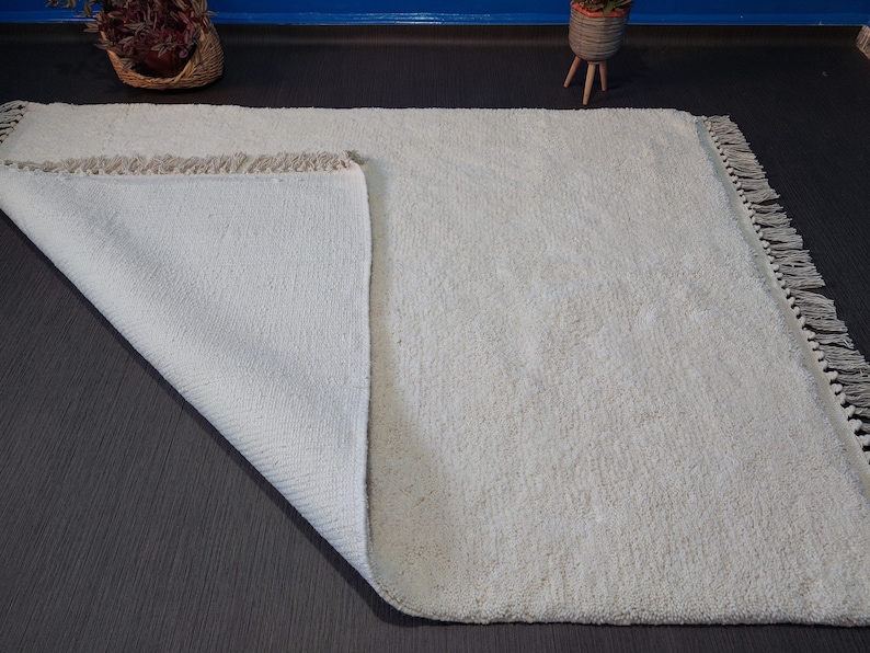 May include: A white, fluffy rug with a fringe border. The rug is folded in half, showing the underside of the rug.