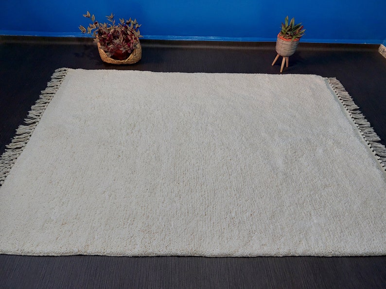 May include: A white shag rug with fringe edging. The rug is on a dark floor.