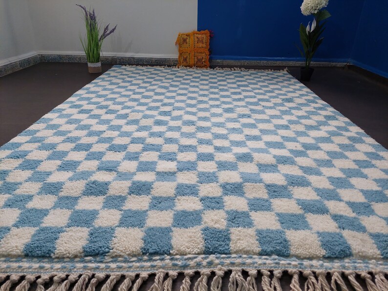 May include: A blue and white checkered rug with a fringe border. The rug is made of a soft, fluffy material.