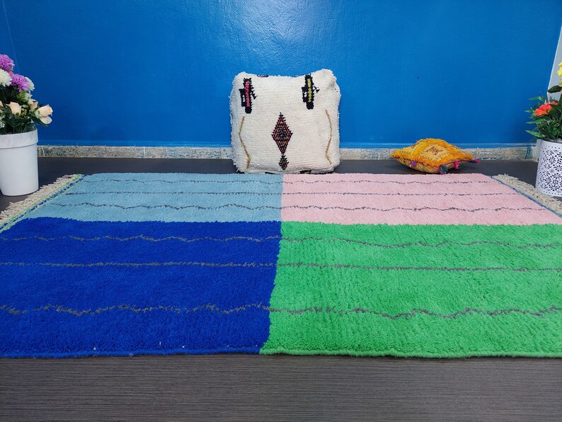 May include: A colorful Moroccan rug with four squares in blue, green, pink, and light blue. The rug is on a dark wood floor with a white pillow with a geometric pattern and a yellow pillow on top of it.