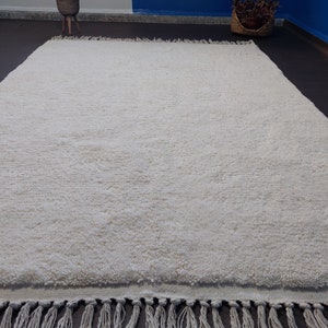 May include: A white shag rug with a fringe border. The rug is made of soft, fluffy fibers and has a subtle texture.