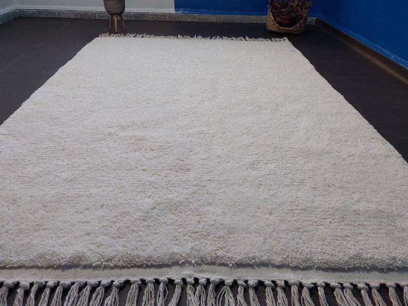 May include: A white shag rug with a fringe border. The rug is made of soft, fluffy fibers and has a subtle texture.