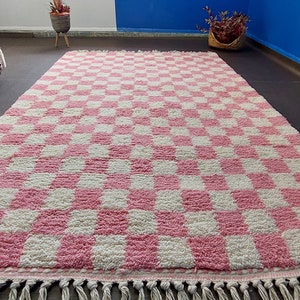 May include: A pink and white checkered rug with fringe on the edges. The rug is made of a soft, fluffy material.