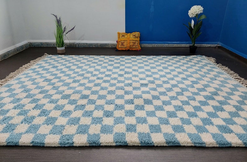 May include: A blue and white checkered rug with fringe edges. The rug is made of a soft, fluffy material.