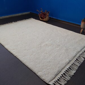 May include: A white shag rug with a fringe border. The rug is on a dark brown floor.