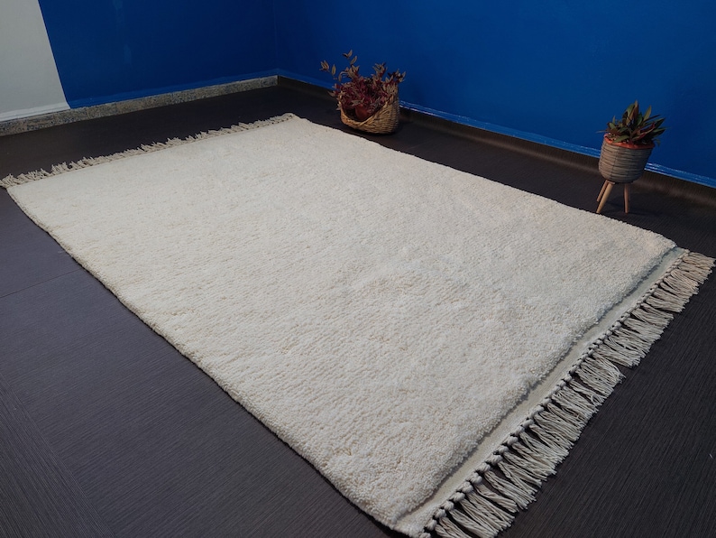 May include: A white shag rug with a fringe border. The rug is on a dark brown floor.