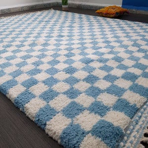 May include: A blue and white checkered rug with a fringe border. The rug is made of a soft, fluffy material.