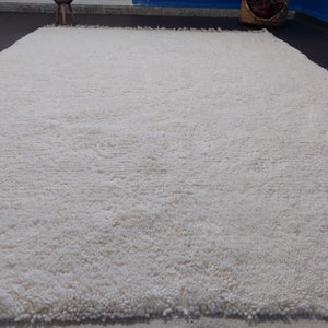 May include: A white shag rug with a fluffy texture. The rug is made of soft, natural fibers and has a simple, elegant design.