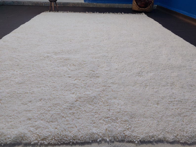 May include: A white shag rug with a fluffy texture. The rug is made of soft, natural fibers and has a simple, elegant design.