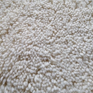 May include: Close-up of a white, fluffy rug with a soft, textured surface.