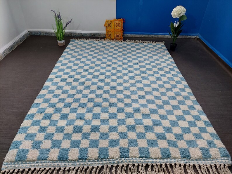 May include: A blue and white checkered rug with a fringe border. The rug is made of a soft, fluffy material.