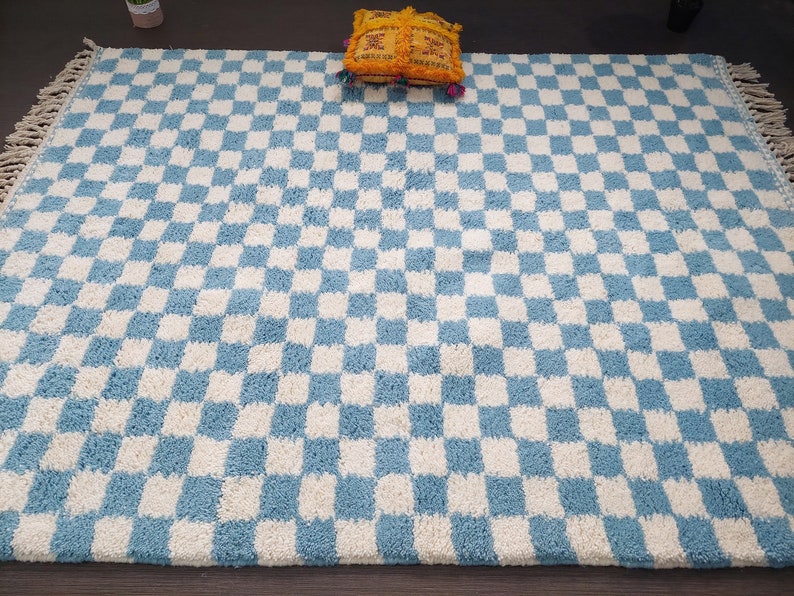 May include: A blue and white checkered rug with a fringe border. The rug is made of a soft, fluffy material.