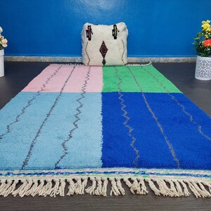 May include: A colorful Moroccan rug with a geometric pattern in shades of pink, blue, green, and white. The rug has a fringe border and is made of wool.