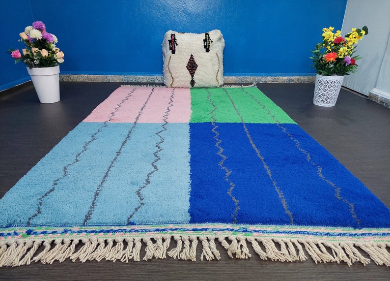 May include: A colorful Moroccan rug with a geometric pattern in shades of pink, blue, green, and white. The rug has a fringe border and is made of wool.