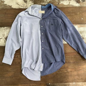 Könnte beinhalten: Ein langärmeliges Hemd mit einem einzigartigen geteilten Design. Eine Hälfte hat vertikale hellblaue Streifen, die andere Hälfte ein blaues Karomuster. Das Hemd hat einen klassischen Kragen und Manschetten, mit dem Markennamen "BLUE WILLOW SHOP" auf dem Etikett.