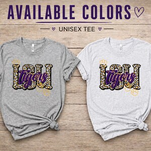 May include: Two unisex t-shirts, one gray and one white, with the text "LSU Tigers" in a leopard print design. The text "AVAILABLE COLORS" is at the top of the image.