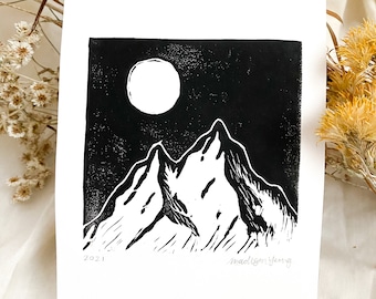 May include: Black and white linocut print of a mountain range with a full moon in the sky. The print is signed "madison yang" and dated "2021".