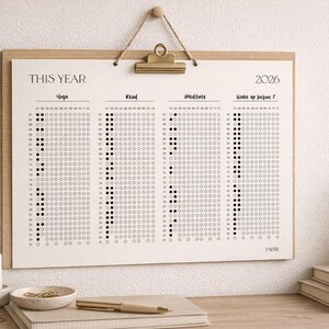 Puede incluir: Un calendario minimalista de seguimiento de h&aacute;bitos para 2026 con el texto "THIS YEAR" en la parte superior. El calendario est&aacute; dividido en secciones para Yoga, Read, Meditate y Wake up before 7. El dise&ntilde;o est&aacute; impreso en papel color crema y enmarcado en madera clara.
