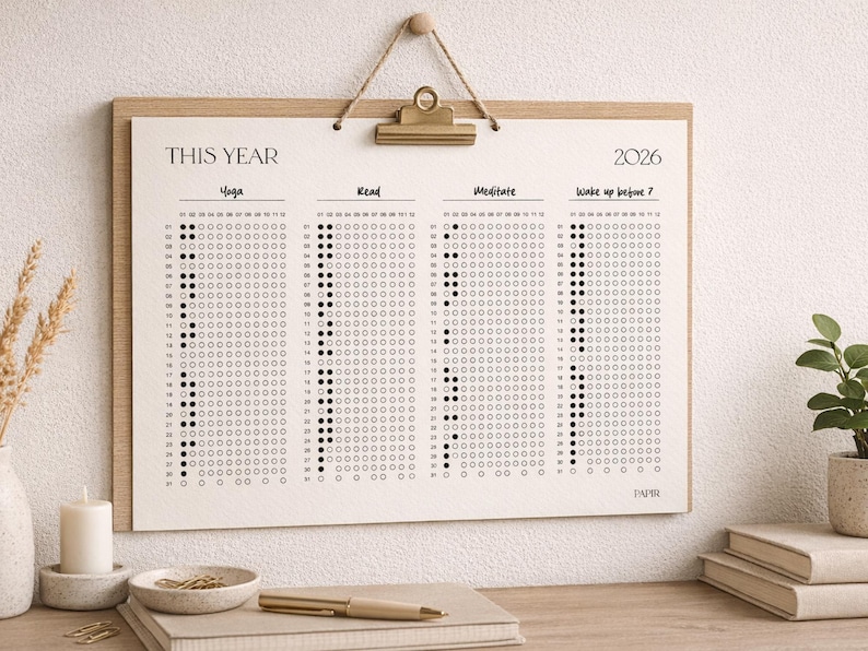 Puede incluir: Un calendario minimalista de seguimiento de h&aacute;bitos para 2026 con el texto "THIS YEAR" en la parte superior. El calendario est&aacute; dividido en secciones para Yoga, Read, Meditate y Wake up before 7. El dise&ntilde;o est&aacute; impreso en papel color crema y enmarcado en madera clara.
