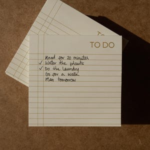 May include: A square off-white to-do list notepad with horizontal lines and a vertical margin line. The text TO DO is printed in the top right corner. Handwritten tasks include Read for 20 minutes, Water the plants, Do the laundry, Go for a walk, and Plan tomorrow.
