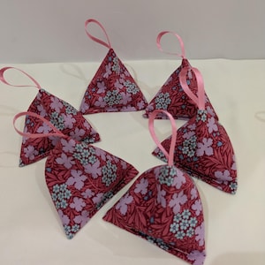 May include: Six pink and red fabric sachets with a floral pattern and pink ribbon ties. The sachets are in the shape of a pyramid.