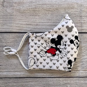 May include: A white face mask with a gray and black Mickey Mouse print. The mask has white elastic straps.