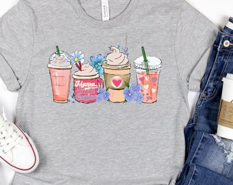 Op de afbeelding: Grijs T-shirt met een afbeelding van drie kopjes koffie met bloemen en de tekst "Mama Needs Coffee".