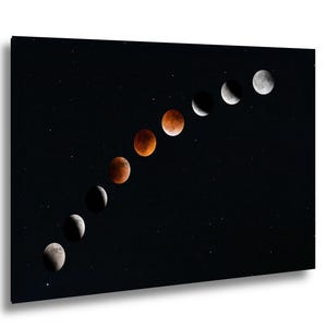 May include: A rectangular wall art print featuring a diagonal sequence of nine lunar phases against a solid black starry sky. The progression transitions from a bright white crescent moon to a deep red total lunar eclipse and back to white.