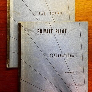 May include: Two vintage books titled "Private Pilot" with light blue covers. The top book reads "FAA Exams" and the bottom book reads "Explanations of Answers". Both books have a stylized wing design and black lines radiating from the bottom.