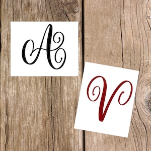 May include: Two white cards with black and red cursive letters. The first card has a black cursive letter "A" with a swirl. The second card has a red cursive letter "V" with a swirl.