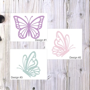May include: Three butterfly designs on white cards against a wood grain background. Design #1 is a lavender butterfly. Design #2 is a pink butterfly. Design #3 is a teal butterfly. Each design has the text "Design #" followed by a number.