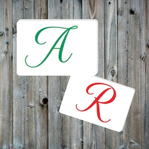 May include: Two white cards with the letters A and R in green and red cursive font, respectively. The cards are on a wood background.
