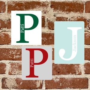 May include: Three personalized initial ornaments with the letters P and J. The ornaments are white, light blue, and gray with green, red, and white letters. The names Patti and Jackson are written on the ornaments.