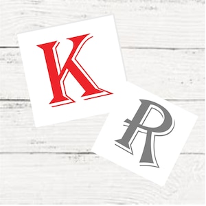 May include: Two decorative letters, a red "K" and a gray "R", are displayed on a white background. The letters are stylized with a bold, serif font.