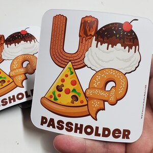 May include: White sticker with a brown, yellow, and white illustration of a pretzel, pizza, churro, and ice cream sundae. The text "Up" and "Passholder" are printed in brown on the sticker.