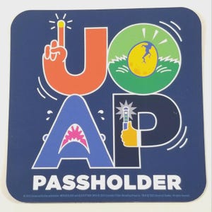 May include: Square blue coaster with the letters "JOAP" in orange, blue, and white, with a green circle and a yellow egg graphic. The word "PASSHOLDER" is at the bottom. The coaster has a fun, cartoonish design.