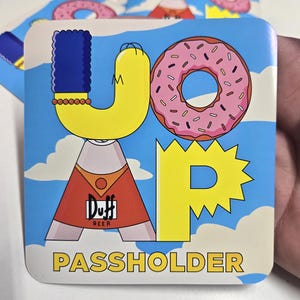 May include: Square coaster featuring a cartoon design with the word "JOAP" in yellow letters, a pink donut, and the text "PASS HOLDER". The design includes a cartoon character in a red shirt with the "Duff Beer" logo.