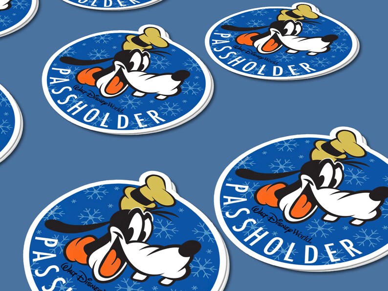 May include: A round blue sticker with a white border features a cartoon image of Goofy wearing a hat and smiling. The background is a blue snowflake pattern. The text "WALT DISNEY WORLD" and "PASSHOLDER" are printed in white on the sticker.