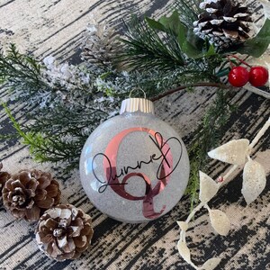 May include: A gray glitter Christmas ornament with a rose gold letter Q and the name "Quinn" written in black cursive.