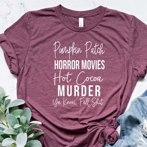 May include: A maroon t-shirt with white text that reads "Pumpkin Patch, Horror Movies, Hot Cocoa, Murder, Ya Know, Fall Shit."