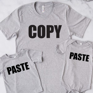 May include: Two gray t-shirts with the words "COPY" and "PASTE" printed on them. The larger shirt has the word "COPY" and the smaller shirt has the word "PASTE".