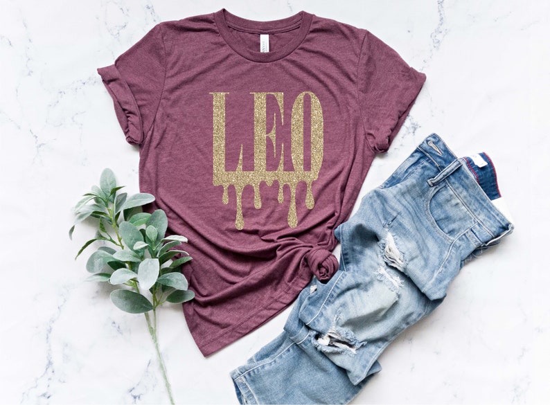 May include: A maroon t-shirt with a gold glitter design that says "LEO" with drips coming from the letters.