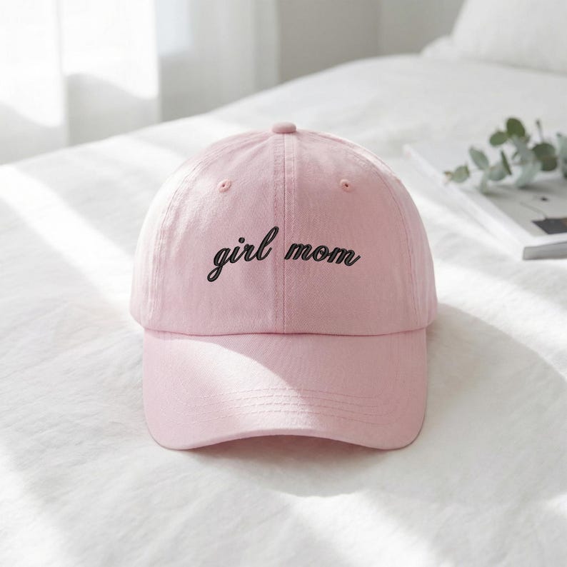 Puede incluir: Gorra de b&eacute;isbol rosa claro con las palabras "girl mom" bordadas en negro. La gorra tiene una visera curva y una corona redondeada. El sombrero est&aacute; hecho de una tela suave.
