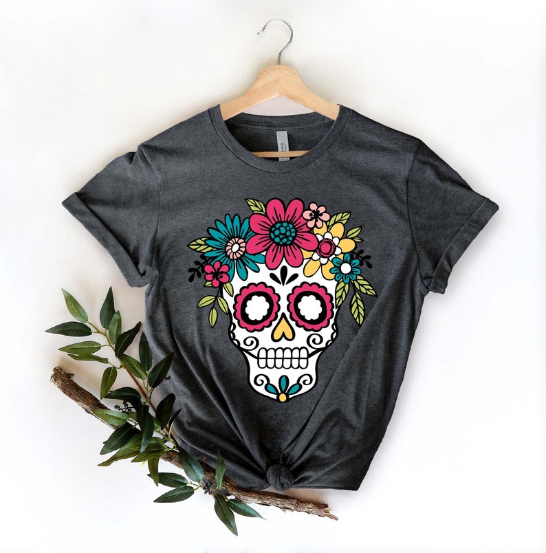 May include: A dark gray t-shirt with a white sugar skull design. The skull is decorated with colorful flowers and has a floral crown.