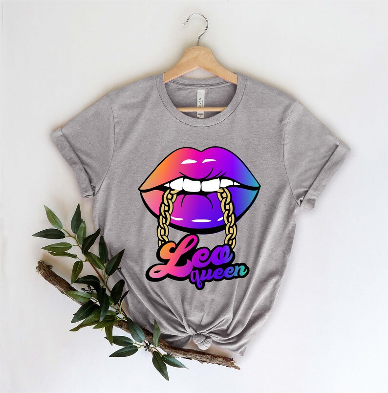 Pu&ograve; includere: Una maglietta grigia con una grafica arcobaleno di un paio di labbra con una catena dorata in bocca. Il testo "Leo queen" &egrave; sotto le labbra.