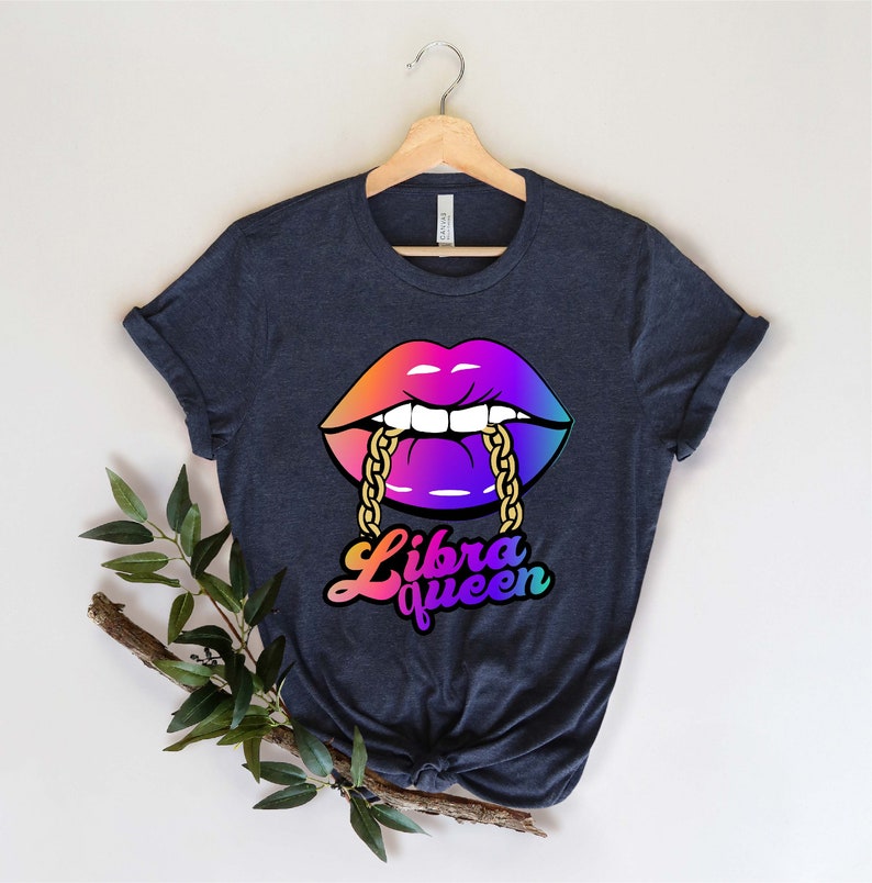 K&ouml;nnte beinhalten: Ein dunkelblaues T-Shirt mit einer regenbogenfarbenen Grafik von einem Paar Lippen mit einer goldenen Kette. Der Text "Libra Queen" ist unter den Lippen in einem Regenbogen-Verlauf geschrieben.
