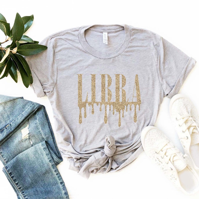 May include: A gray t-shirt with the word "LIBRA" in gold glitter lettering. The letters are dripping with gold glitter.