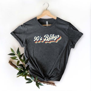 May include: A dark gray t-shirt with a retro-style graphic that says "90's Baby" in rainbow colors.