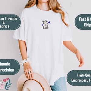 May include: White t-shirt with an embroidered West Highland White Terrier and two blue butterflies. The shirt features the text "Premium Threads & Fabrics", "Handmade With Precision", "Made With Love", and "High-Quality Embroidery Finishing".